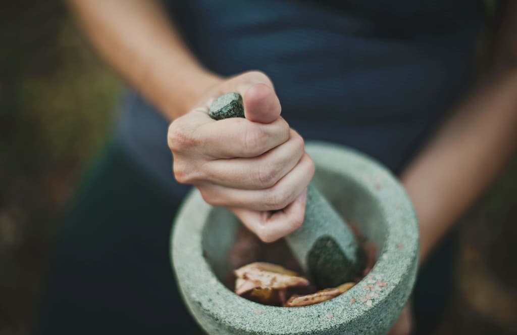 manos preparando una mezcla de hojas y pétalos en un cuenco de piedra